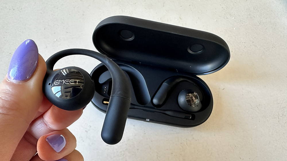Someone holding an Emeet AirFlow earbud with another one in the charging case