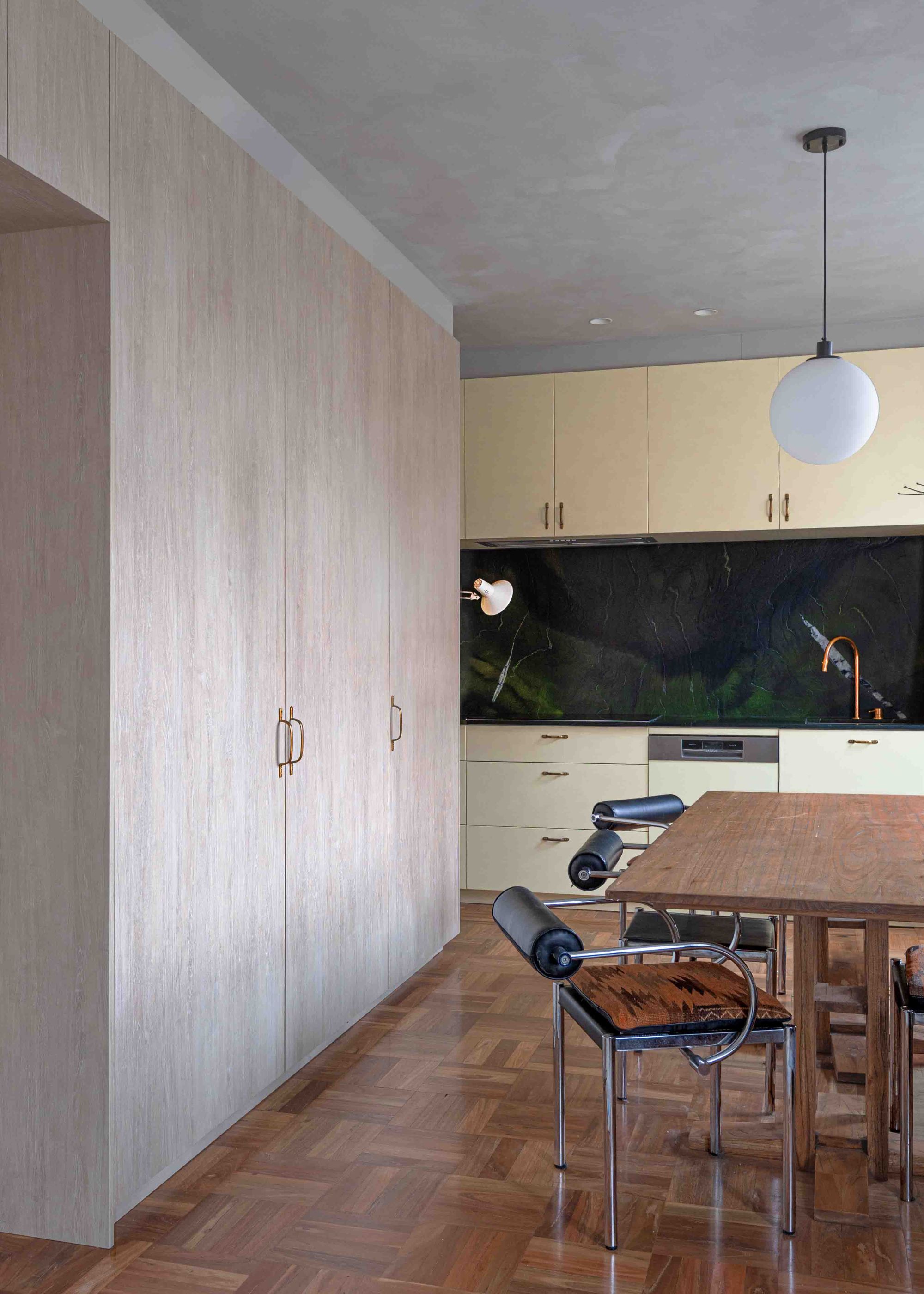 A kitchen and dining room with yellow cabinets, wood cupboards, a wood dining table, leather and steel chairs, and a green marble backsplash