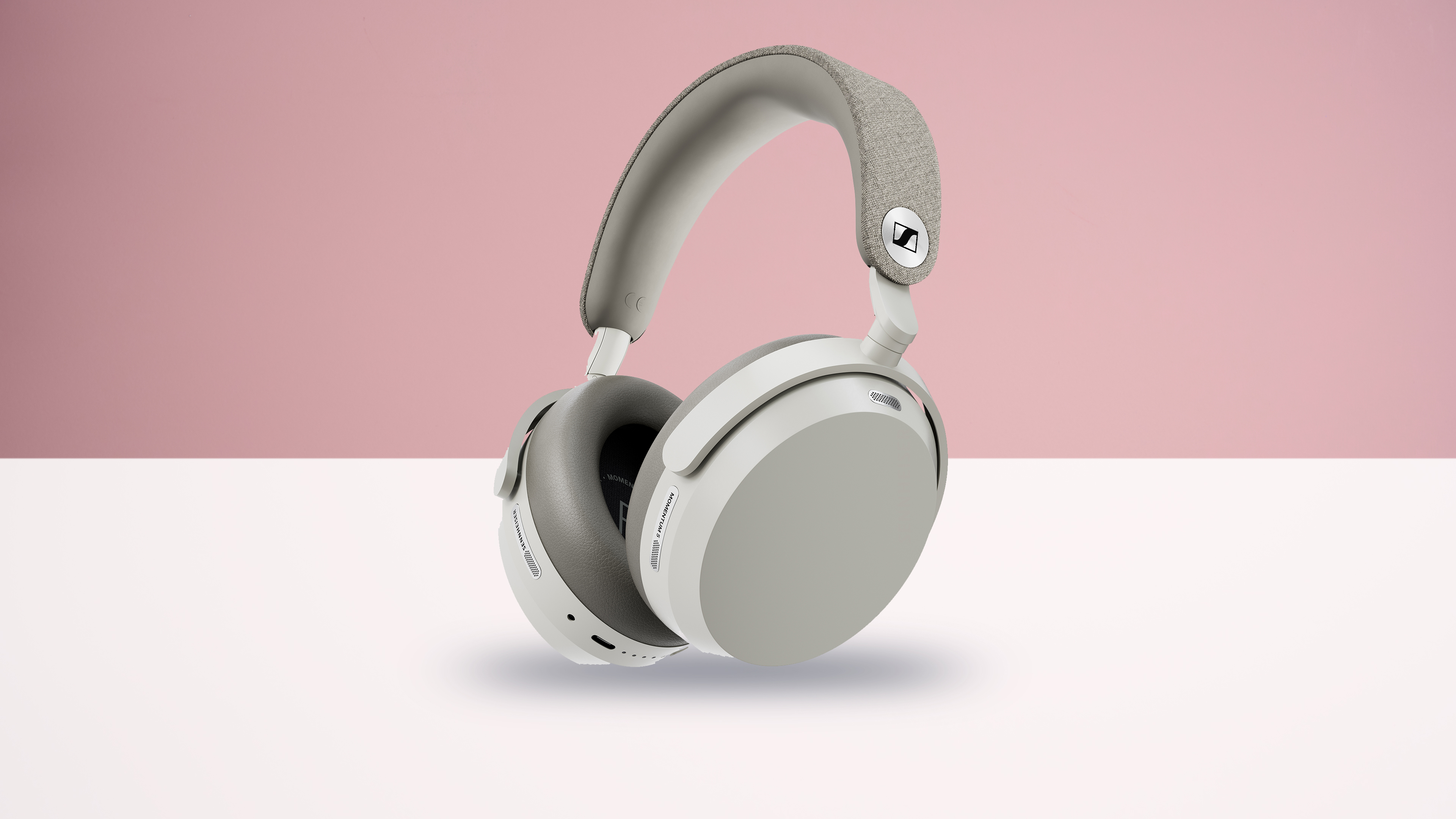 The Sennheiser Momentum 5 Wireless headphones on a white surface with a pink background