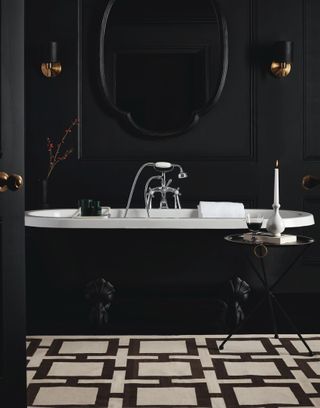 A black bathroom with a black bath next to a black and white rug below a black mirror