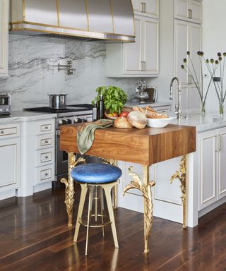 A kitchen with a marble island and antique wooden butchers block with turquoise leather and brass stool