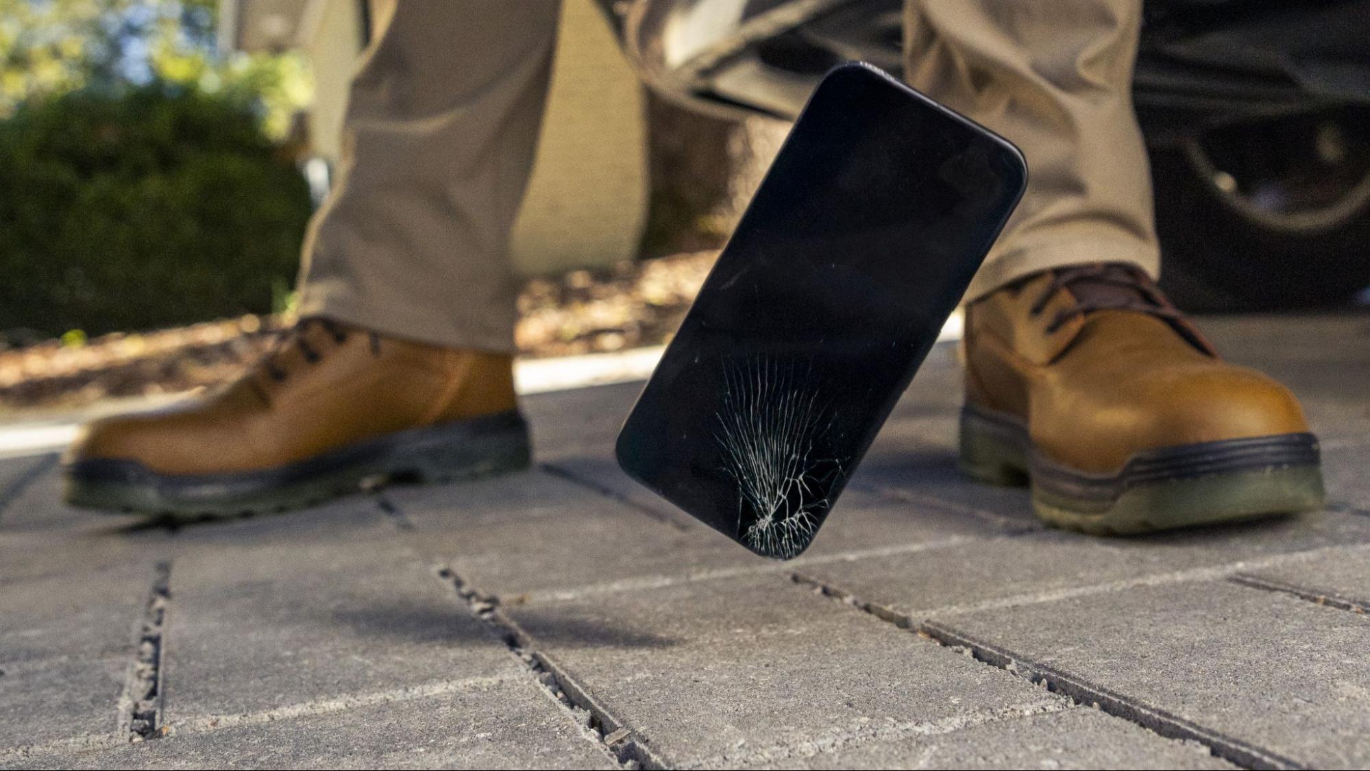 A phone falling and breaking on the sidewalk.