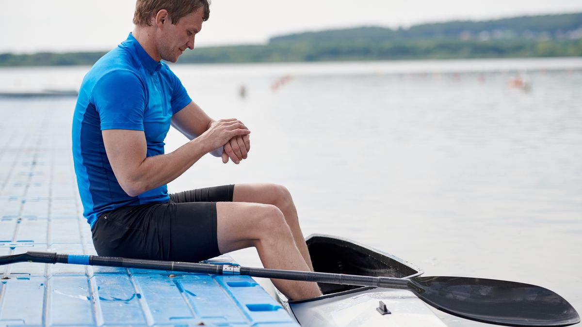 Man sitting on quay with feet in kayak checking sports watch