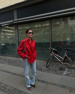 Annabel wears a red shirt, ripped jeans, and black sandals.