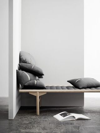 Daybed by Anita Johansen for Menu. A daybed with a wooden frame and black seat in the corner.