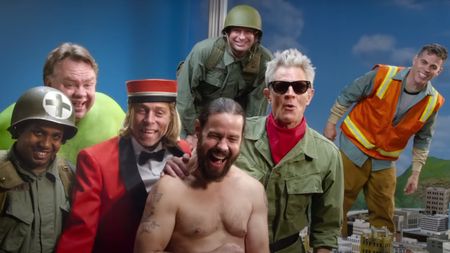 The cast of Jackass Forever stand smiling in the miniature city scene.