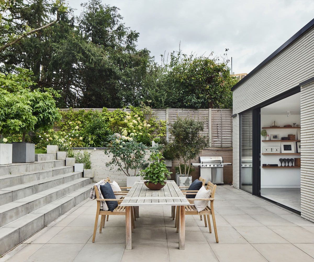A table in a garden with a raised garden behind with hydrangeas and surrounded by grey slabs