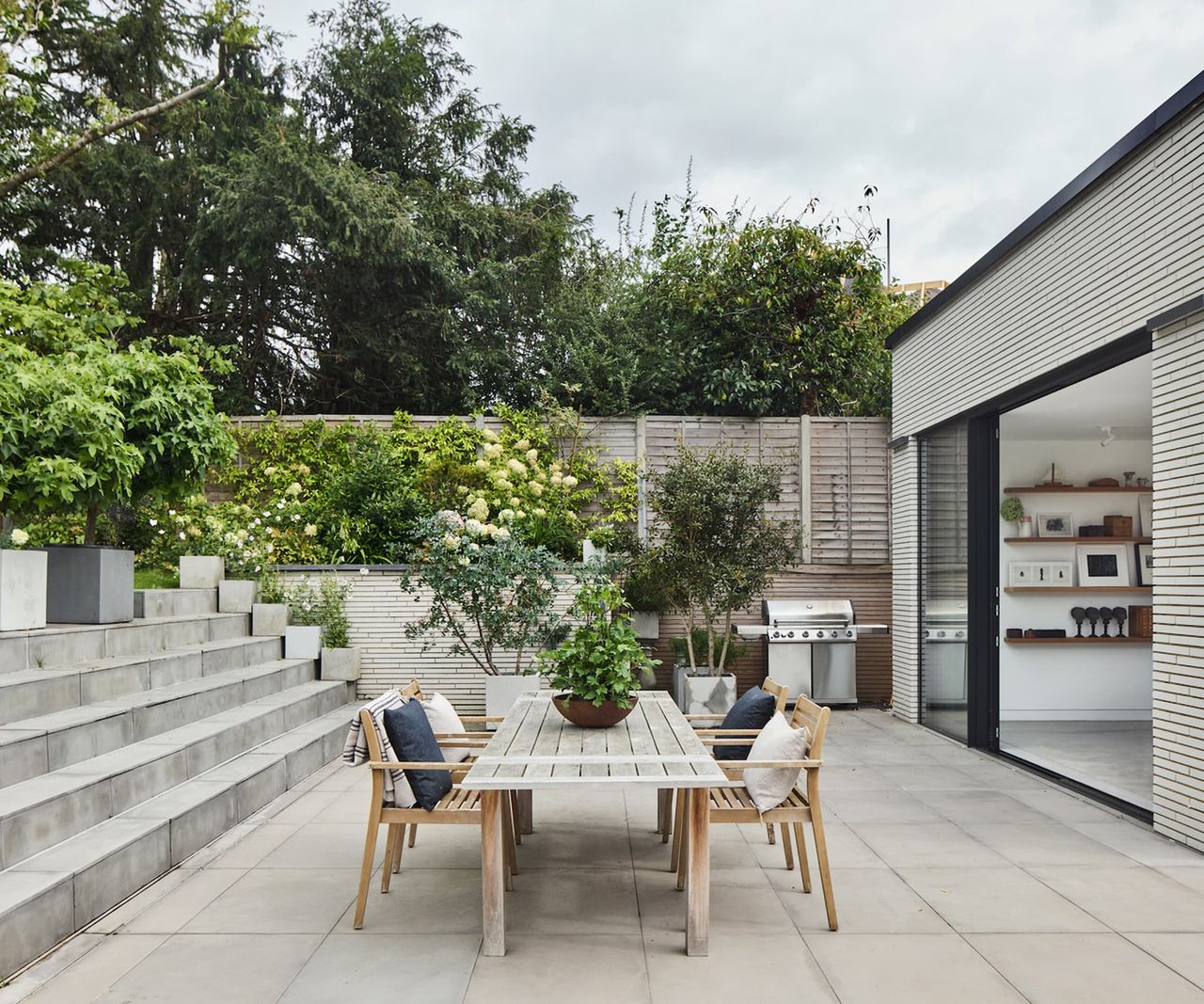 A table in a garden with a raised garden behind with hydrangeas and surrounded by grey slabs