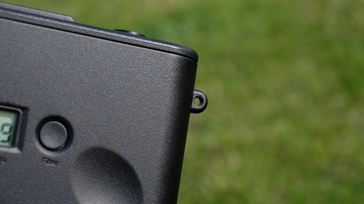 Photograph of man's hand holding Camp Snap 2 digital camera, in yellow colorway, showing close view of lug hole for strap attachment