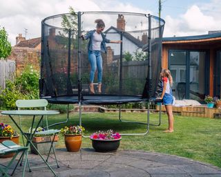 Two older girls playing around a trampoline in a garden