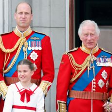 Prince William and King Charles wear red military uniforms as they stand on the Buckingham Palace balcony