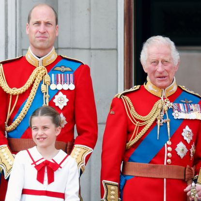 Prince William and King Charles wear red military uniforms as they stand on the Buckingham Palace balcony