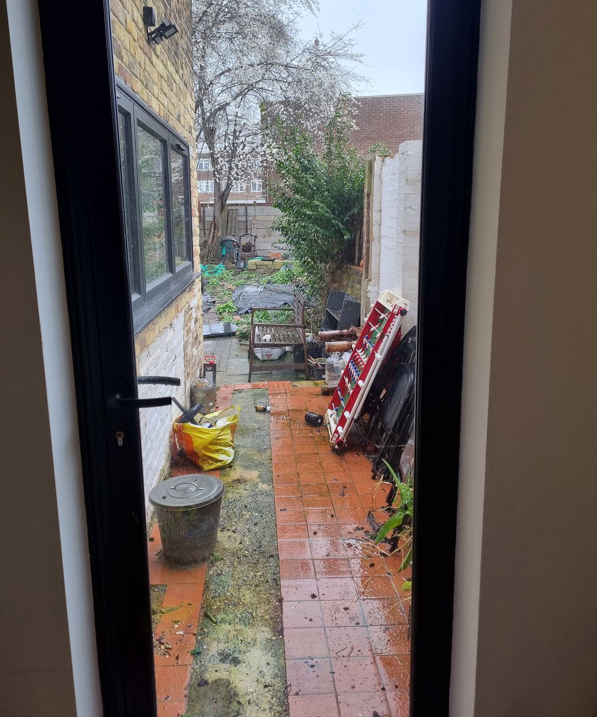 A side return patio in a poor condition with lots of clutter and bad paving