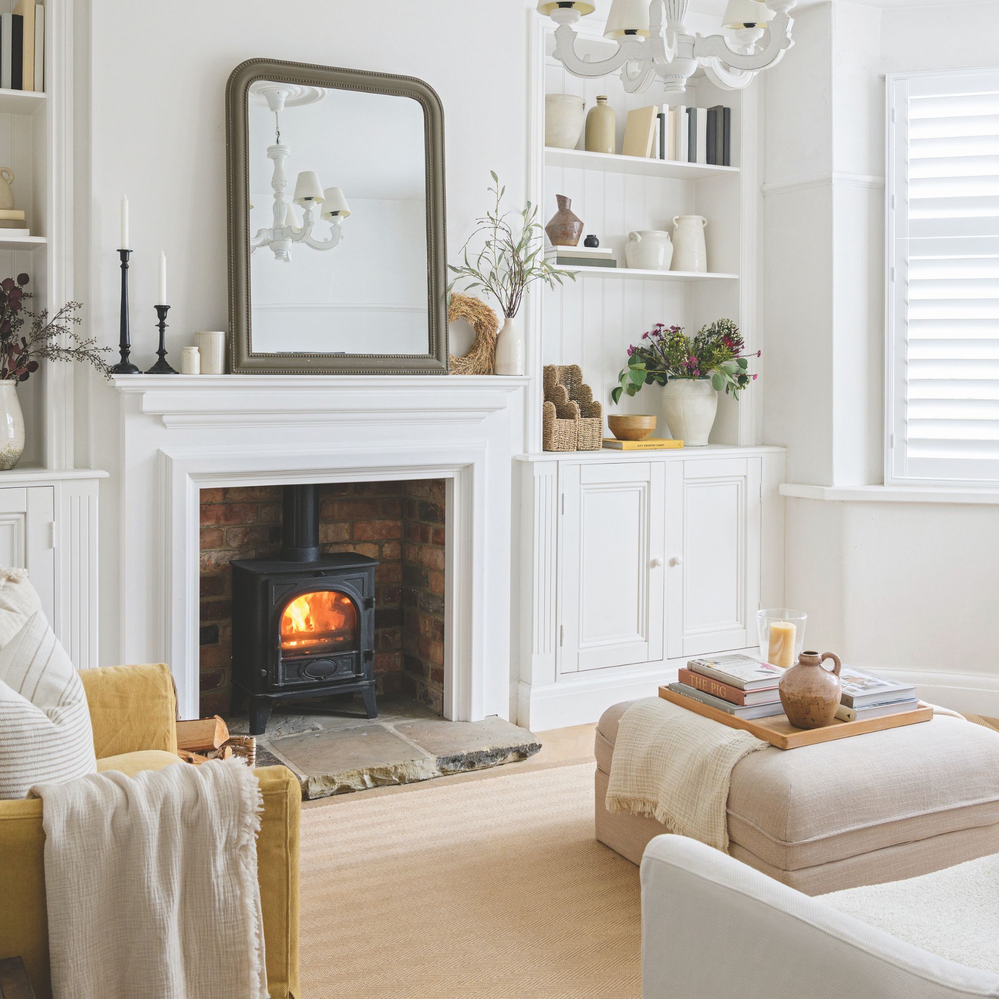 White living room with log burner, a white mantle with a mirror on it, a cream rug and footstool on it