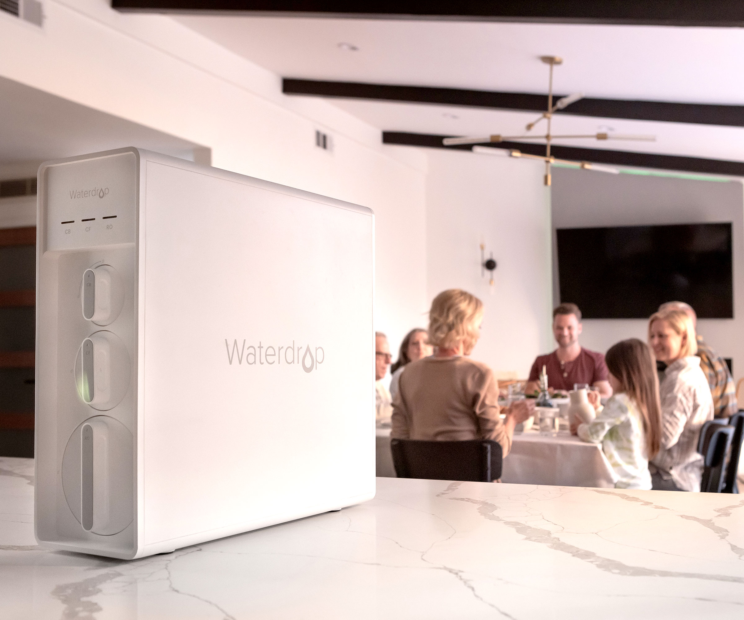 Waterdrop Filter X12 countertop system on marble top with family in background in white dining area with black beams