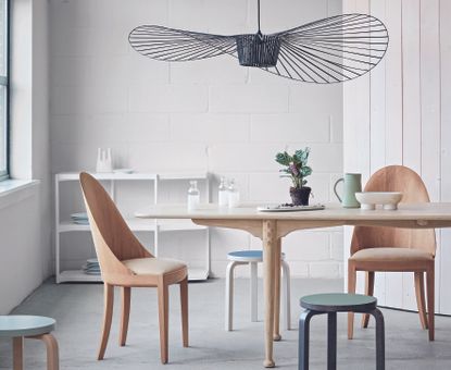 Dining area with polished concrete floor, wooden table, chairs and stools, white painted brick wall and wood panel.