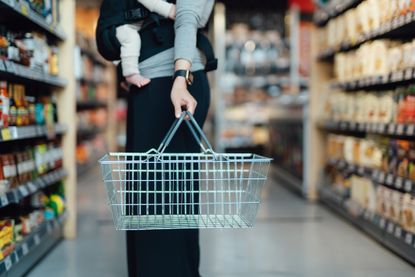 Mother carrying baby and a shopping basket in supermarket