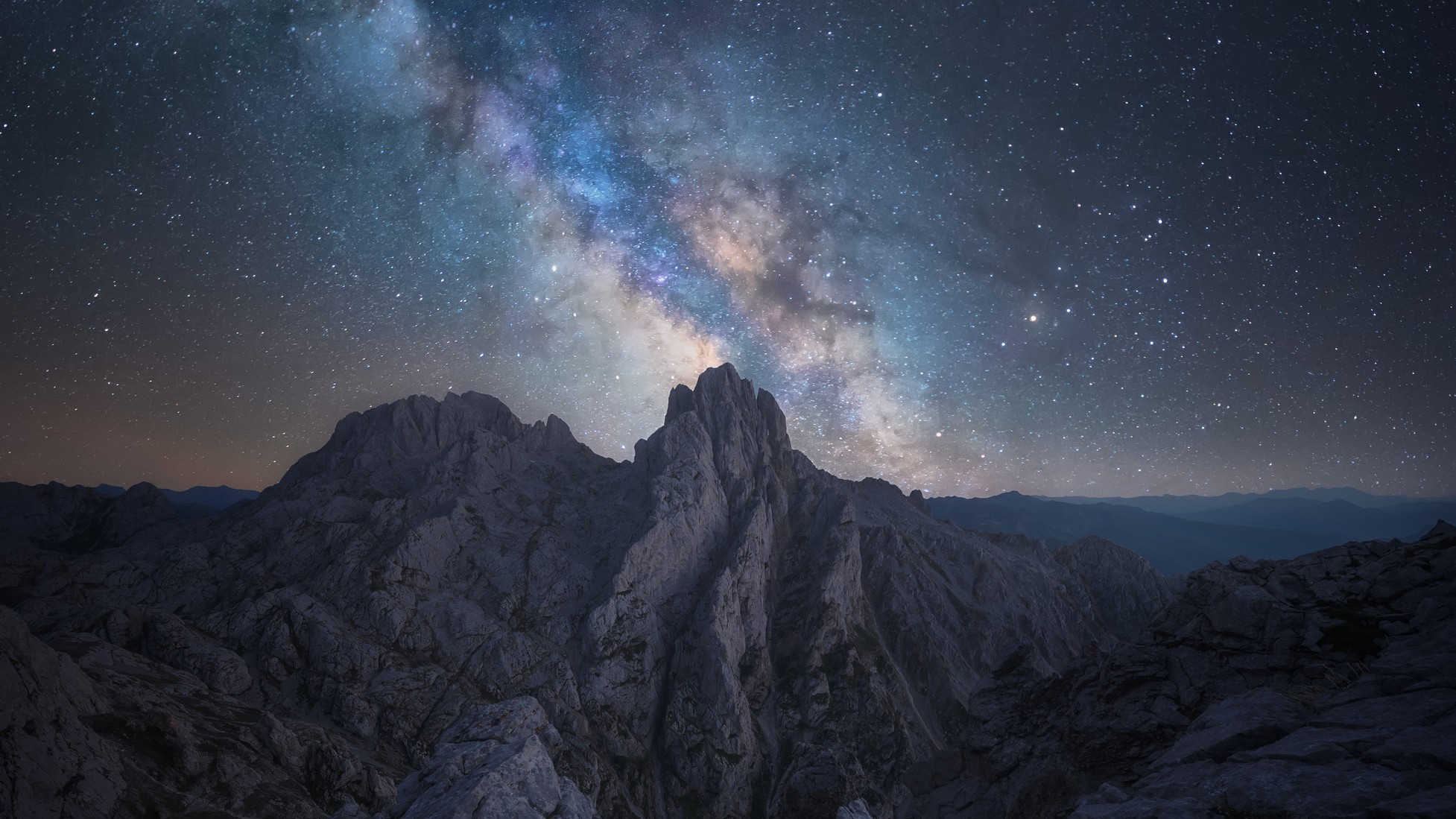 milky way streaking over a rock formation against a background of stars.