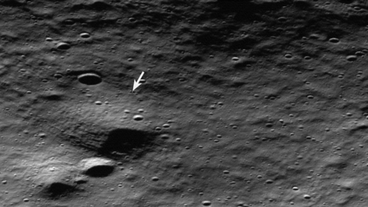 spacecraft photo of the cratered lunar surface, with a white arrow pointing to the location of a moon lander inside a small crater