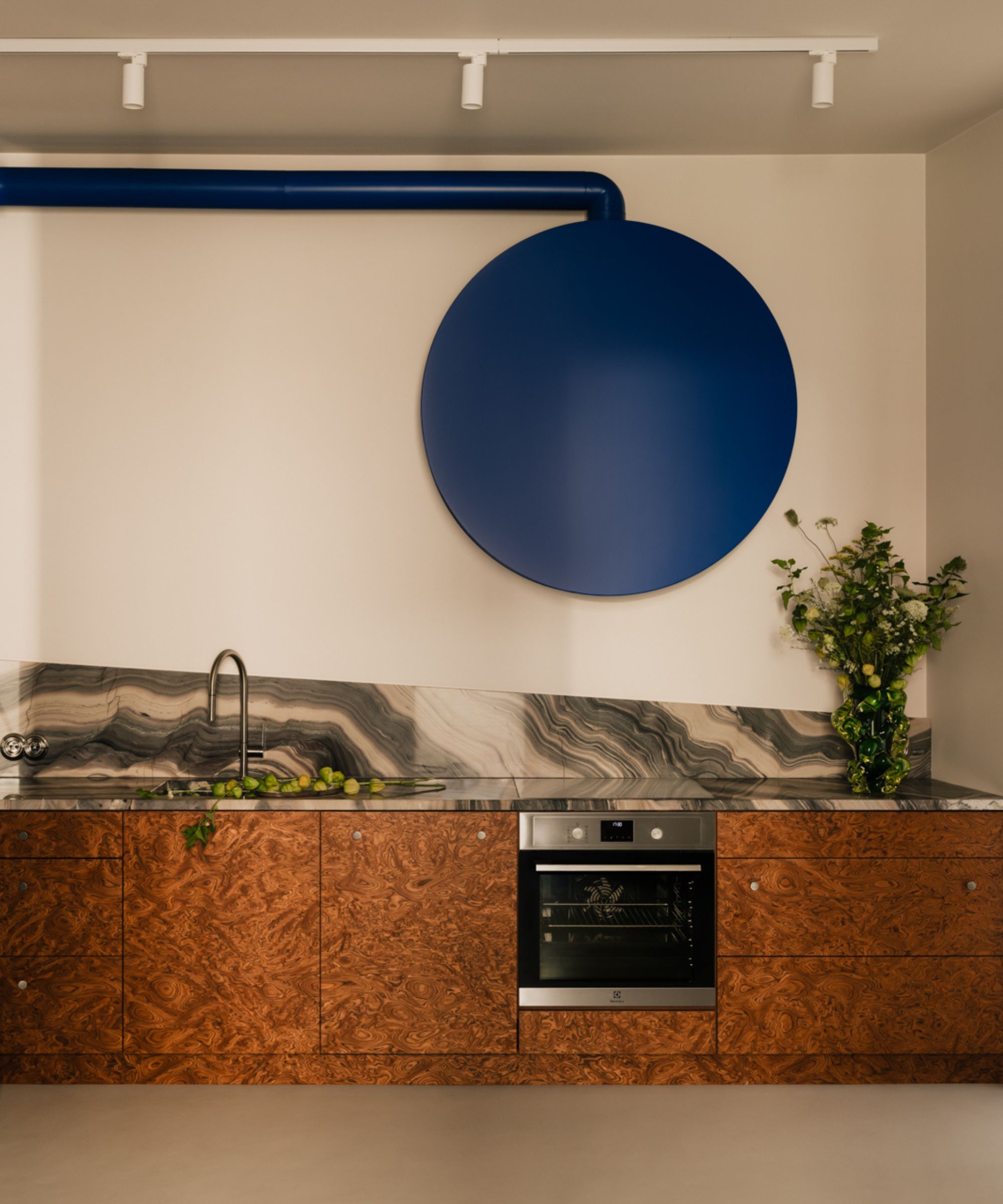 a kitchen with burl wood base cabinets, a marble countertop and backsplash, a blue range hood, and white walls