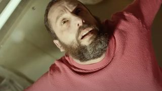 Close up of a bearded man in a red sweater throwing back his hands whilst looking upwards.