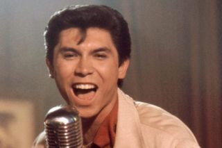 Lou Phillips Diamond as Ritchie Valens singing into a microphone in 50s clothing in la bamba