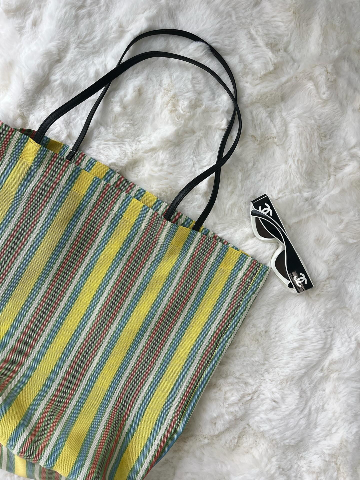 Flatlay photo of The Row striped mesh market tote with black and white Chanel sunglasses.
