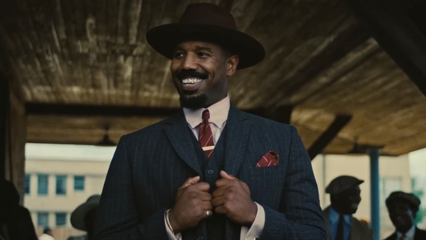 Michael B Jordan holds his suit jacket as he smiles proudly in Sinners. 