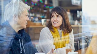Woman talking to a friend in person in a cafe, wearing yellow scarf, representative of how to help someone with burnout