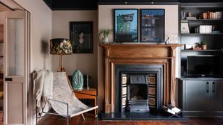 living room in Victorian home with plaster pink walls, wooden fireplace with tiled surround, built in dark grey storage units, wooden floors and modern metal framed occasional chair