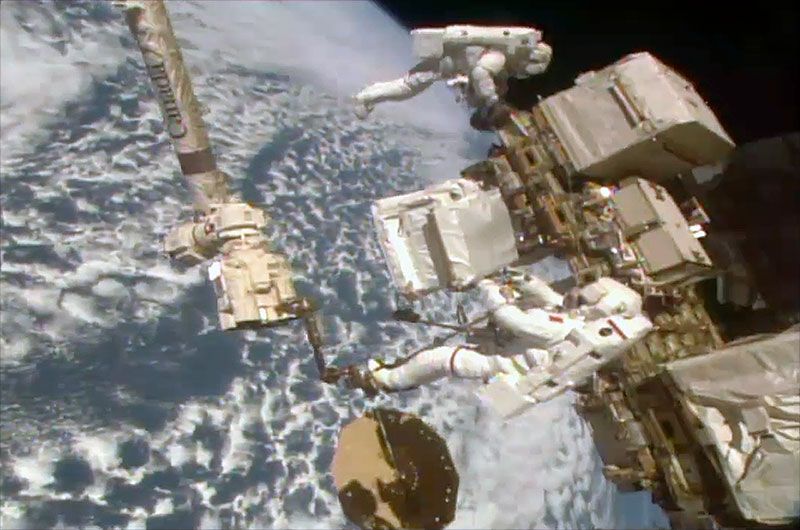 Astronauts Luca Parmitano (in foreground) and Drew Morgan work outside the International Space Station on Dec. 2, 2019. Parmitano, positioned at the end of the station&#039;s Canadarm2 robotic arm, is holding the new pump module for the Alpha Magnetic Spectrometer cosmic ray detector.