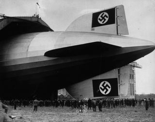 The ill-fated German airship "Hindenburg" (LZ-129) being maneuvered into a hangar. Two swastikas, symbols of the German National Socialist Party, are displayed on its tail.