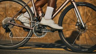 A black man rides a gold bike with black Hunt's new 32 Aerodynamicist wheels down a sunlit road