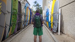 Person wearing a dry bag on a street lined with paddle boards