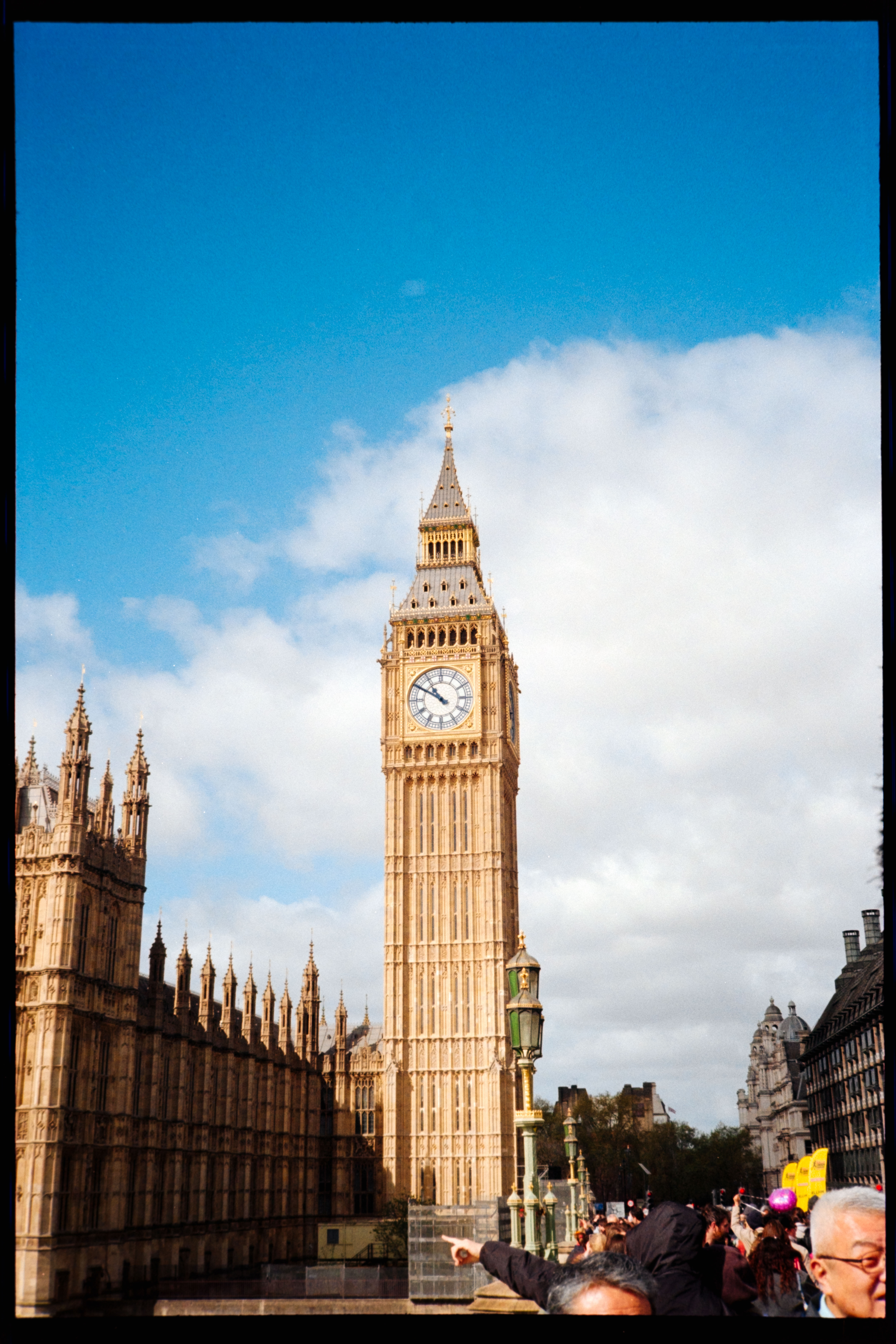 Elizabeth Tower and the Houses of Parliament in London under a partly cloudy sky, with crowds in the foreground.