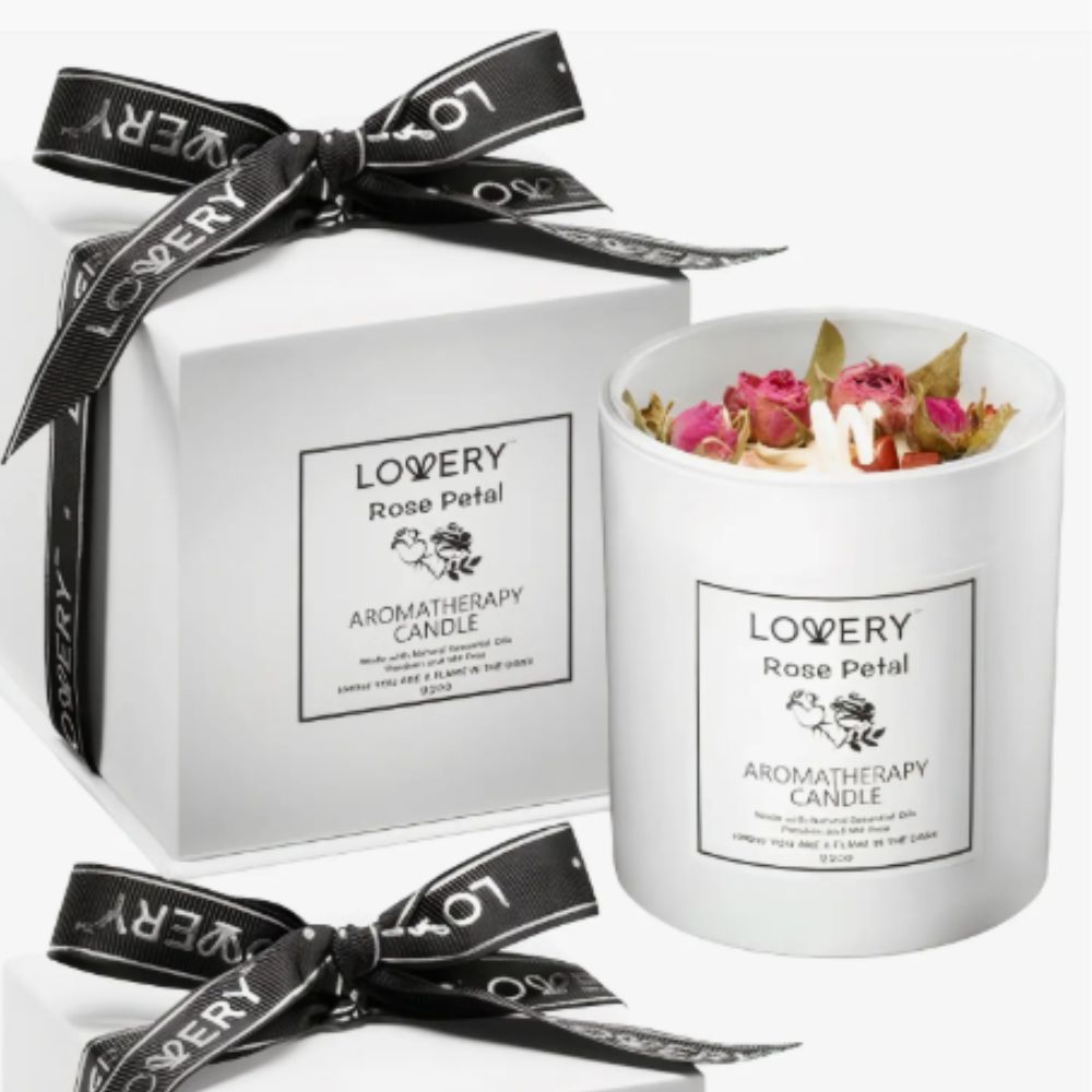 Rose petal candle in white pot next to white gift box tied with black ribbon