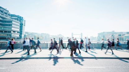 A group of people in work clothes walking over a bridge in a city. 