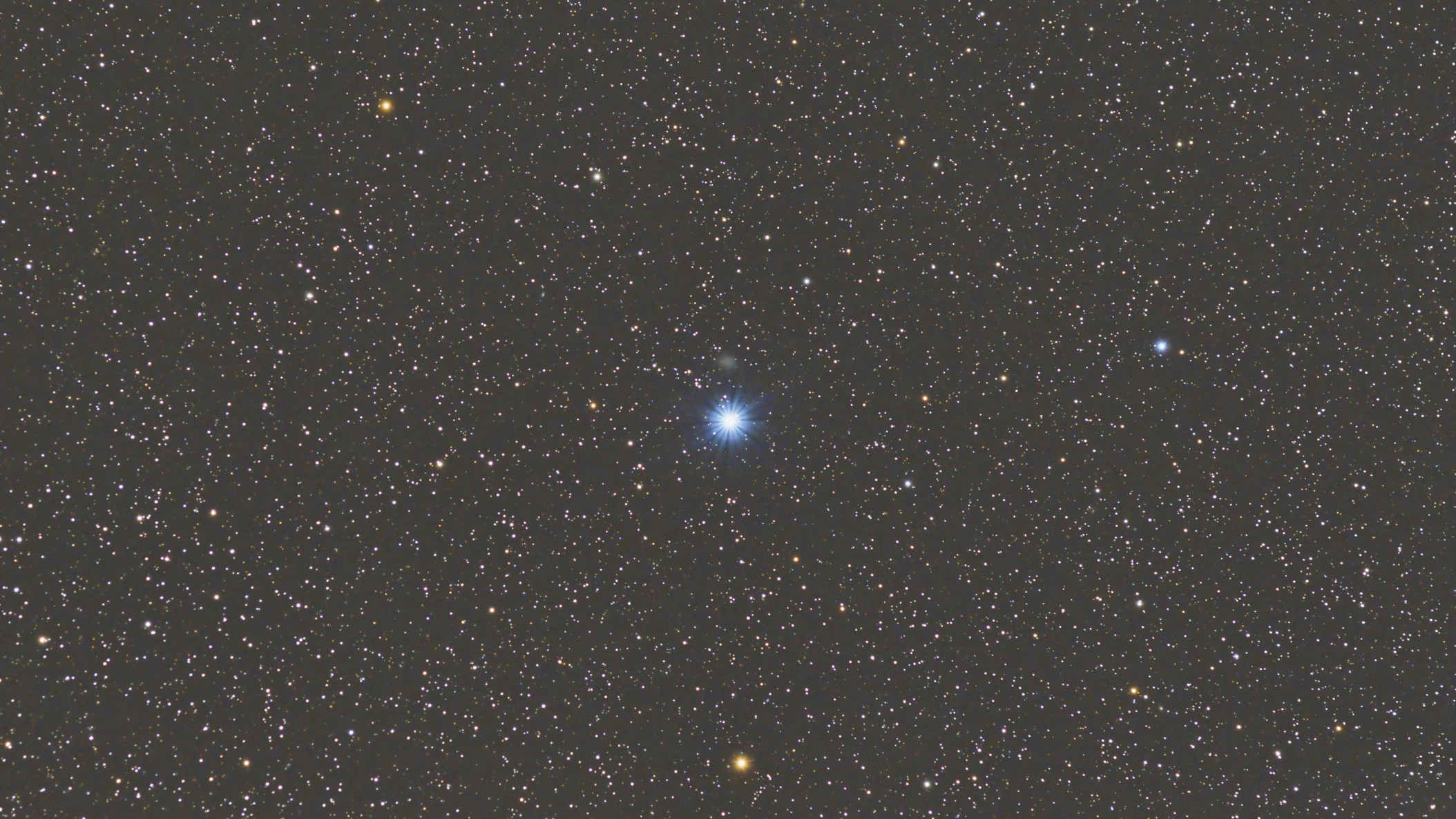 night sky image showing a bright blue star in the center, surrounded by thousands of smaller stars ranging from yellow, orange, blue and white in color.