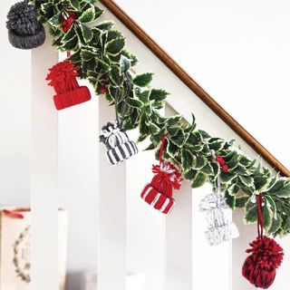 Knitted Christmas hats hanging on green garland on wooden balustrade