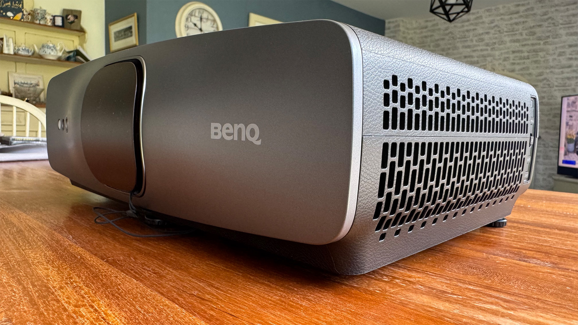 The BenQ W2720i projector, pictured on a wooden table in a living room