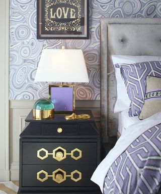 A teenage girl bedroom idea with purple marble-inspired wallpaper, and graphic patterned purple bedding with black side table