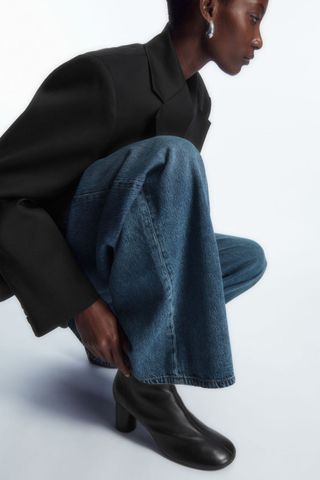cos sale - woman crouched down touching her black ankle boots wearing jeans and a jacket