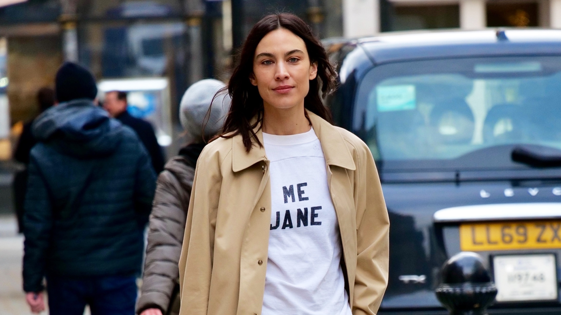 Alexa Chung wearing a trench coat, white T-shirt, army green utility pants, and metallic pink kitten heels in London