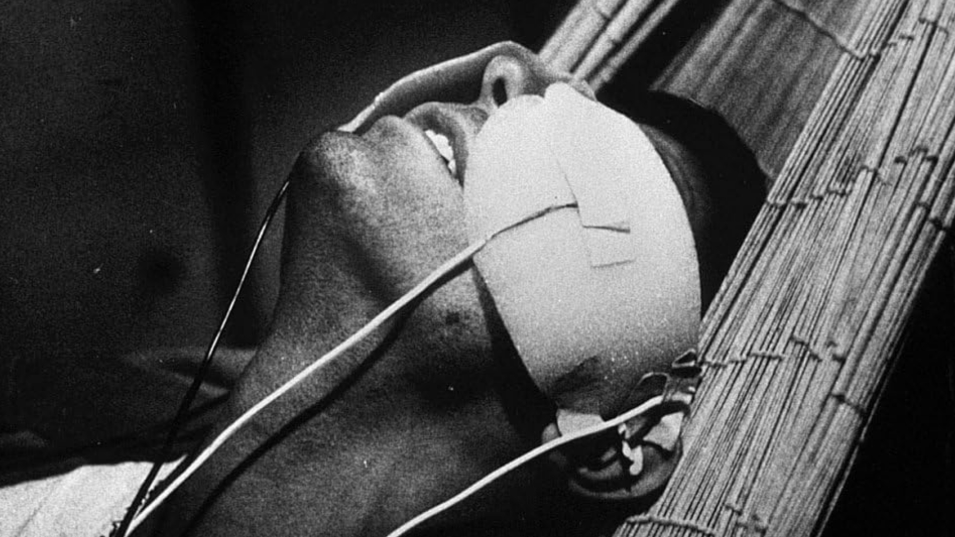 A man lays on a hammock with coverings over his eyes that have wires connected to them