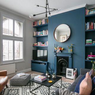 Living room with one blue and one grey painted wall and round mirror above fireplace