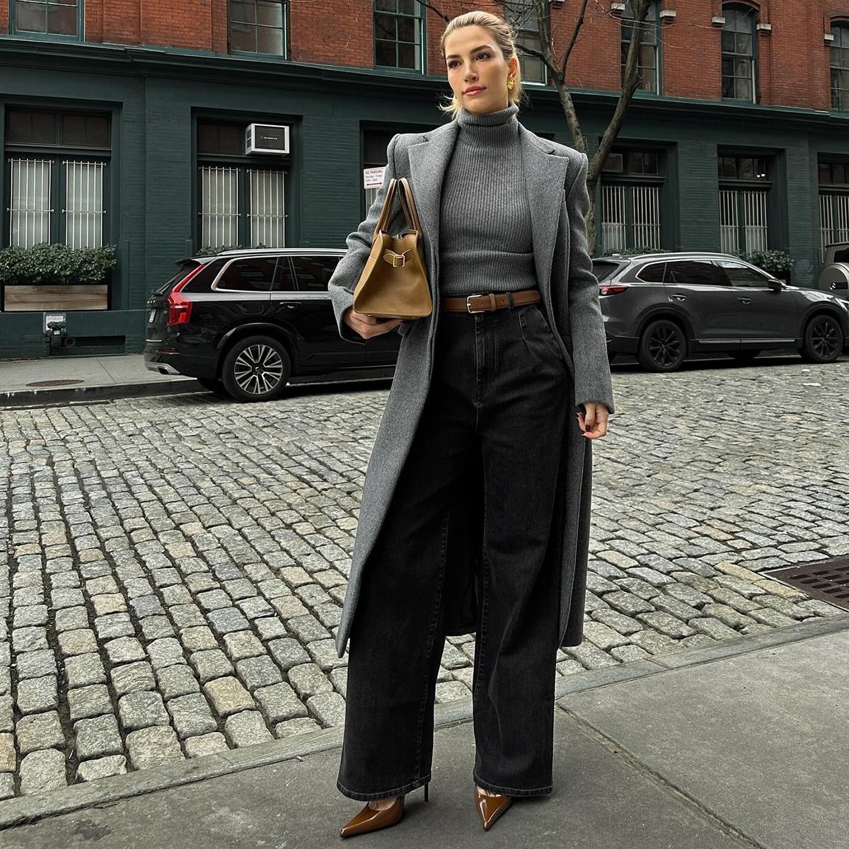 Cass wears a gray turtleneck, gray coat, beige belt, and black jeans