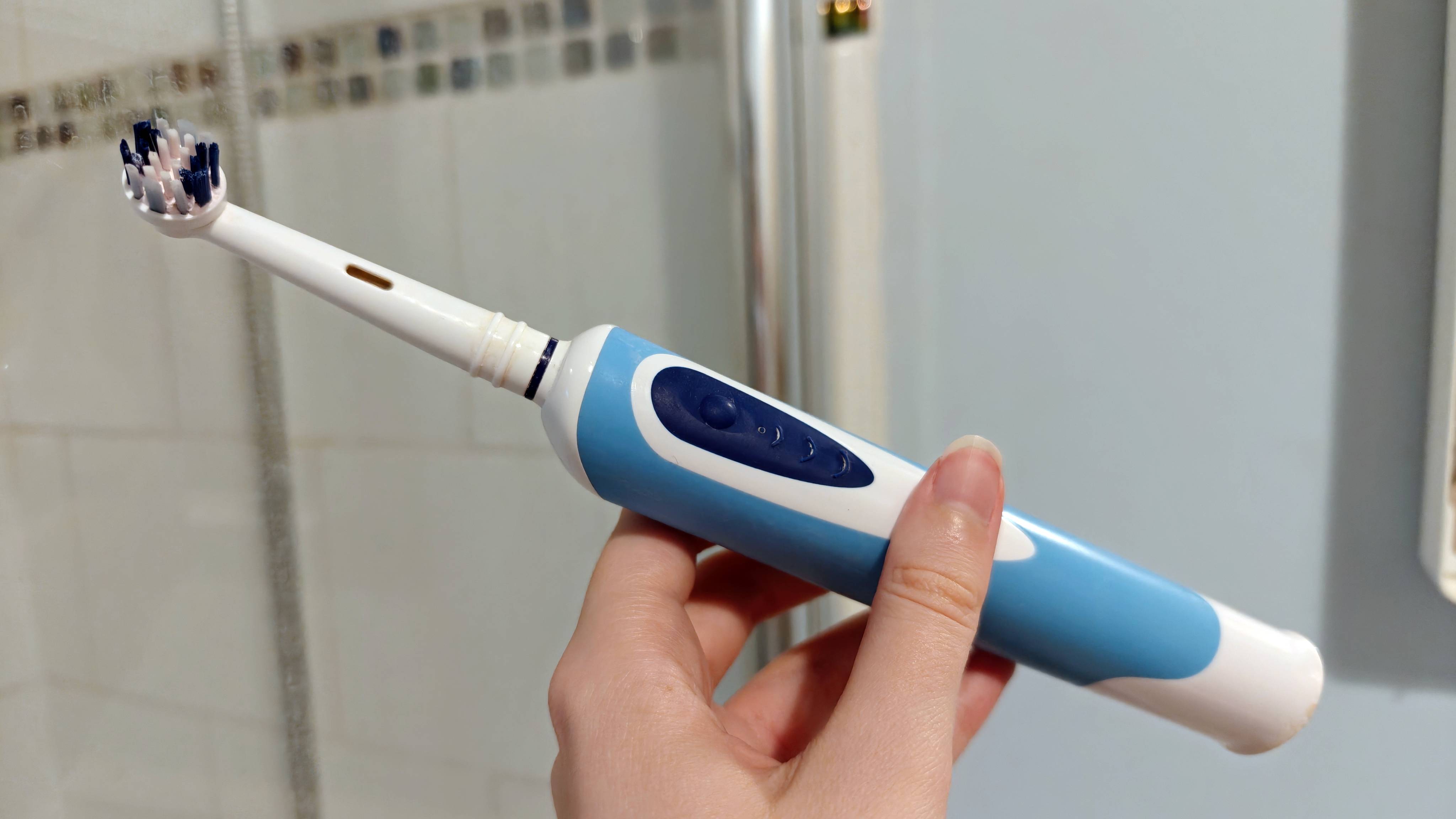 Electric toothbrush held in hand, in a bathroom