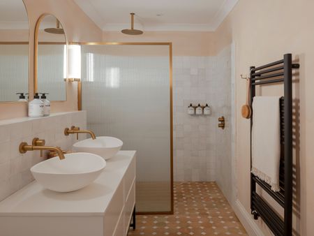 an ensuite bathroom with a double vanity basin, walk in shower and walls and floors in earthy tiles and muted walls