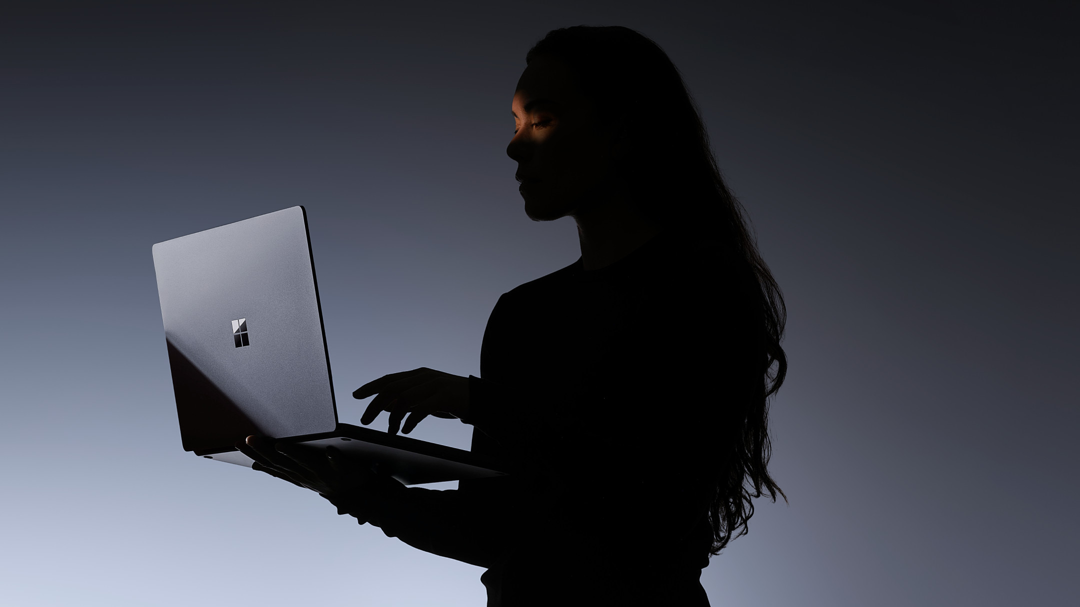 Microsoft Surface Laptop Ultra laptop open, being held by a person in very shadowed lighting