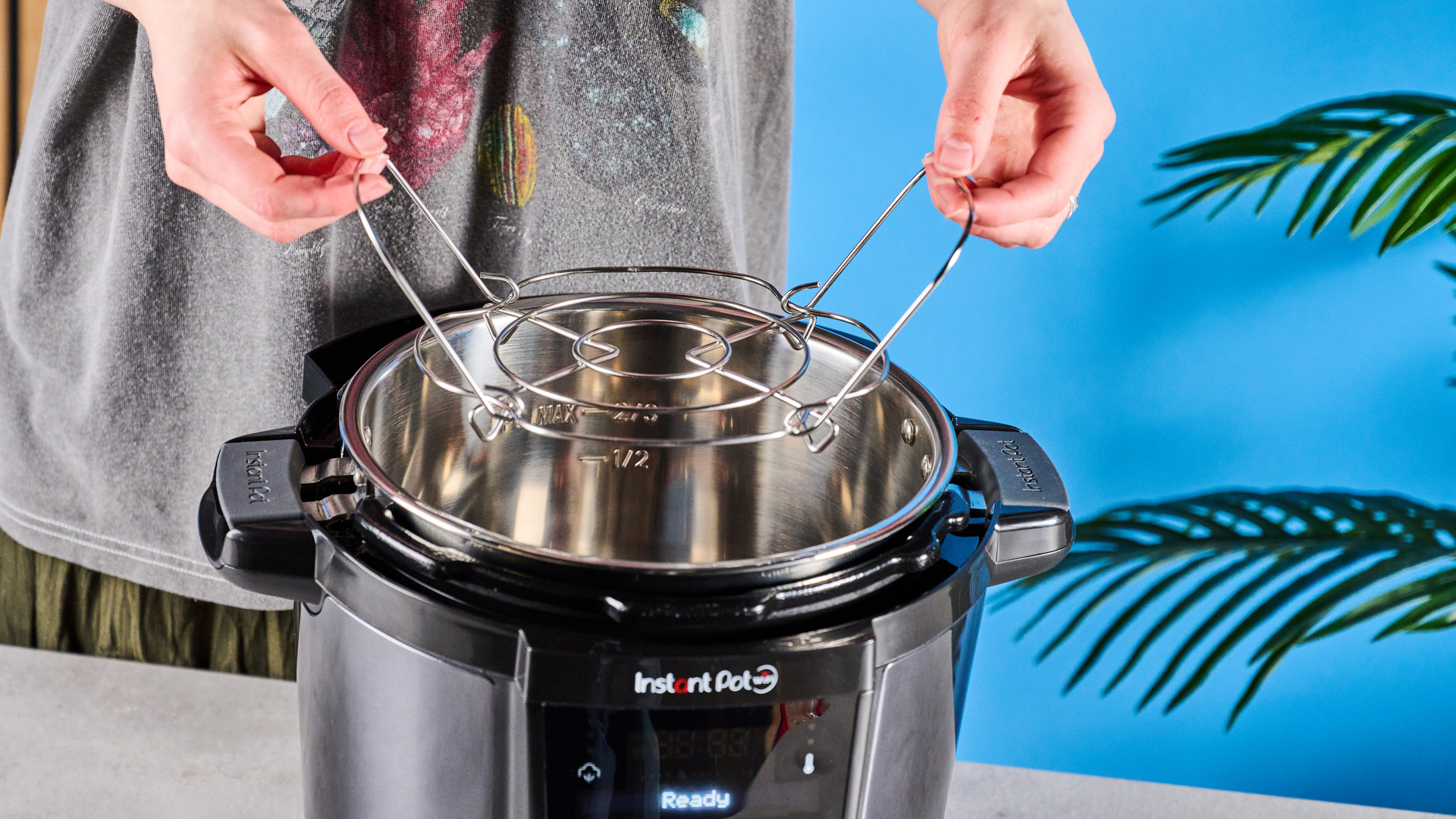 Instant Pot Plus photographed in front of a blue background.